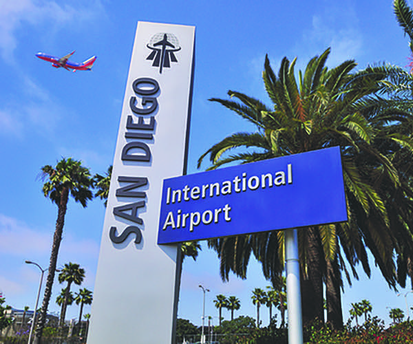 Sign of the san Diego Interantional Airport with a plane flying in the background