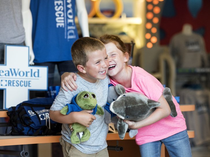Two young kids hug while holding stuffed animals at SeaWorld San Diego.