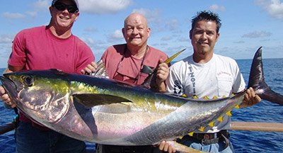 Three guys caught a yellowtail fish and are displaying it proudly