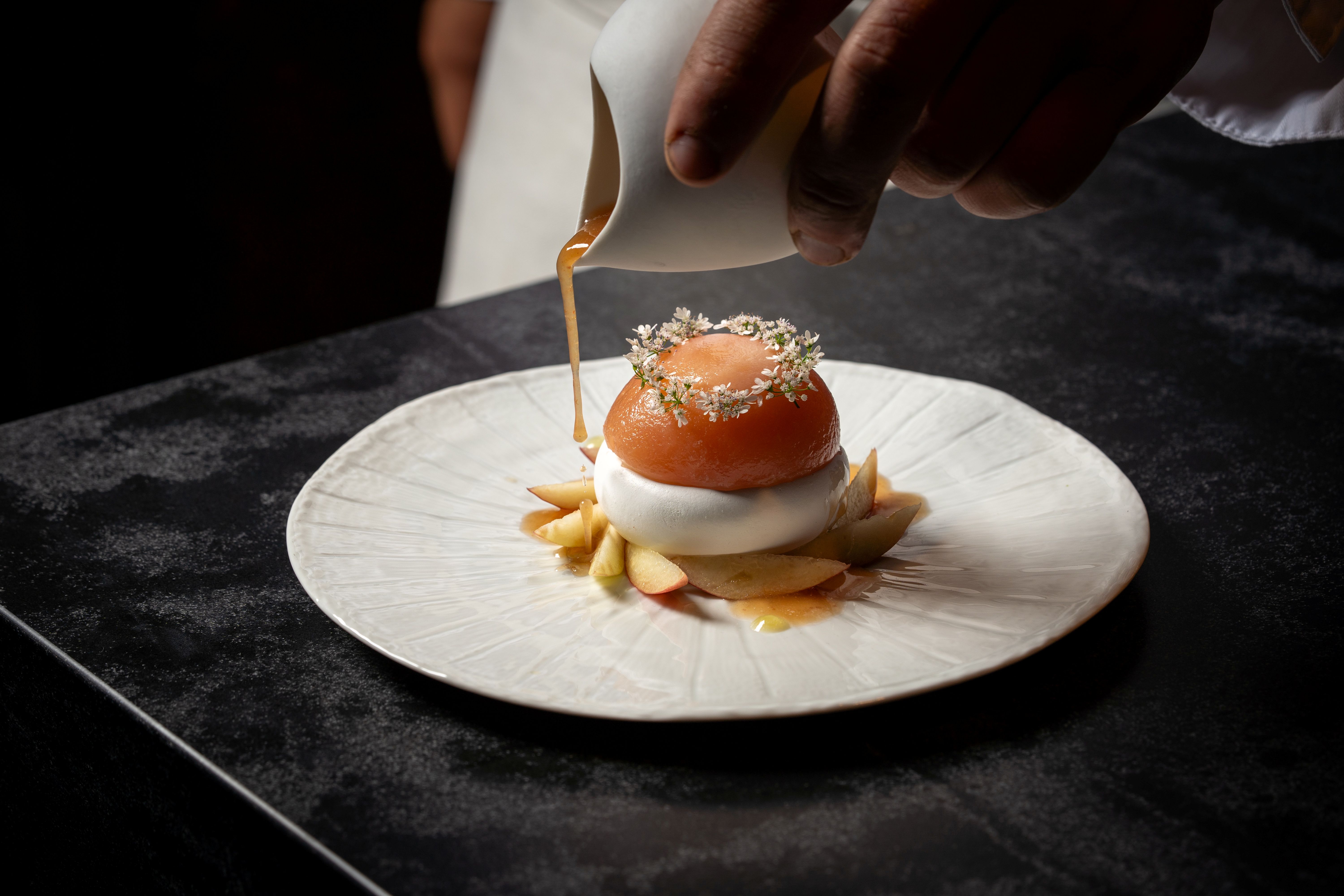 A chef drizzles sauce over a beautifully plated dessert with apples and a garnished dome at Lucien, a restaurant in the San Diego community of La Jolla.