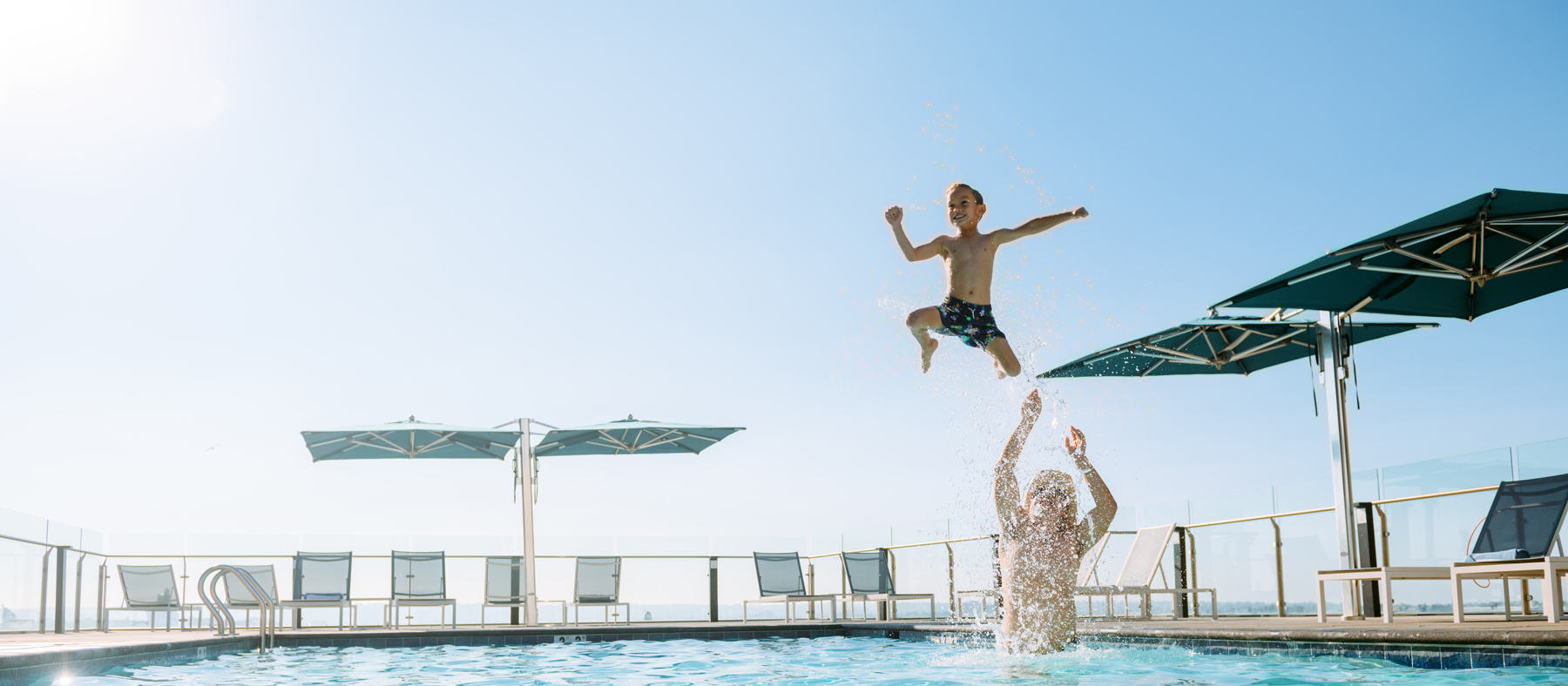 Kid jumps into mans arms splashing on rooftop pool in San Diego, CA