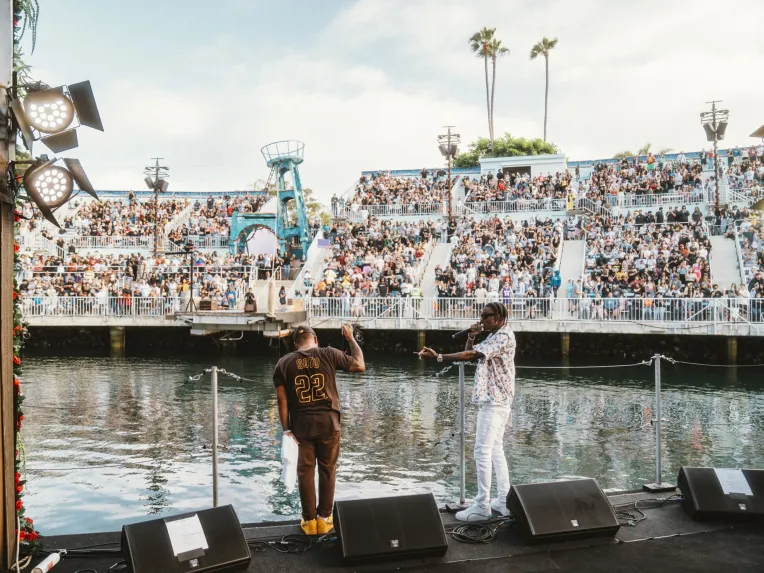 Soulja Boy and Bow Wow on stage for the SeaWorld San Diego Summer Concert Series in front of a large crowd by a waterfront venue.