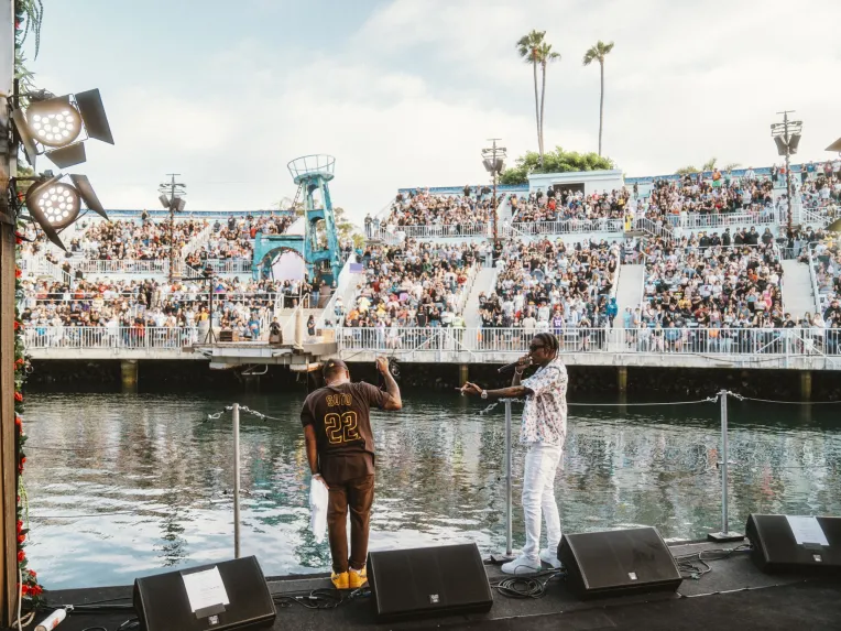 Soulja Boy and Bow Wow on stage for the SeaWorld San Diego Summer Concert Series in front of a large crowd by a waterfront venue.