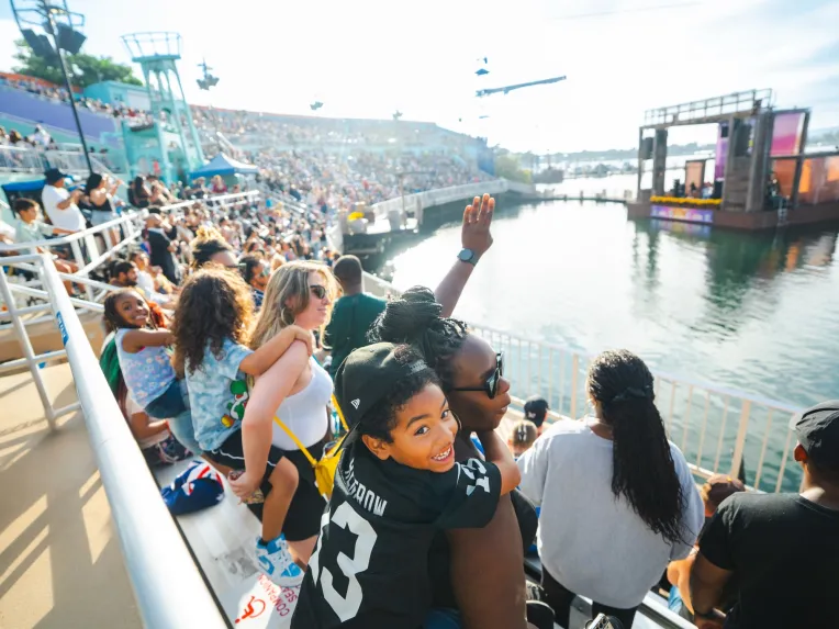 A diverse crowd watches a SeaWorld San Diego Summer Concert by the water, with excitement and smiles visible.