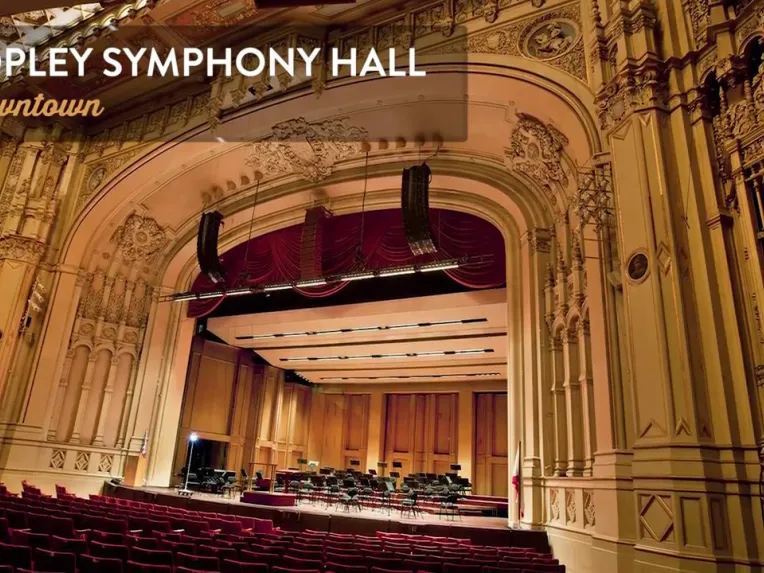 Elegant interior of Copley Symphony Hall with ornate architectural details, red seats, and an empty stage set for an orchestra performance.