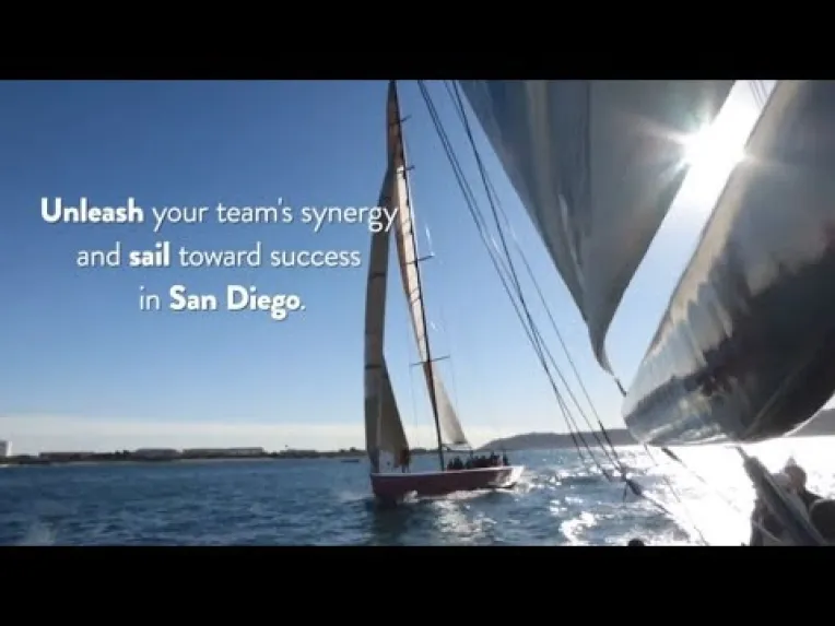 A sailboat on the water near San Diego with people onboard; text overlay promotes team synergy and success through sailing in San Diego.