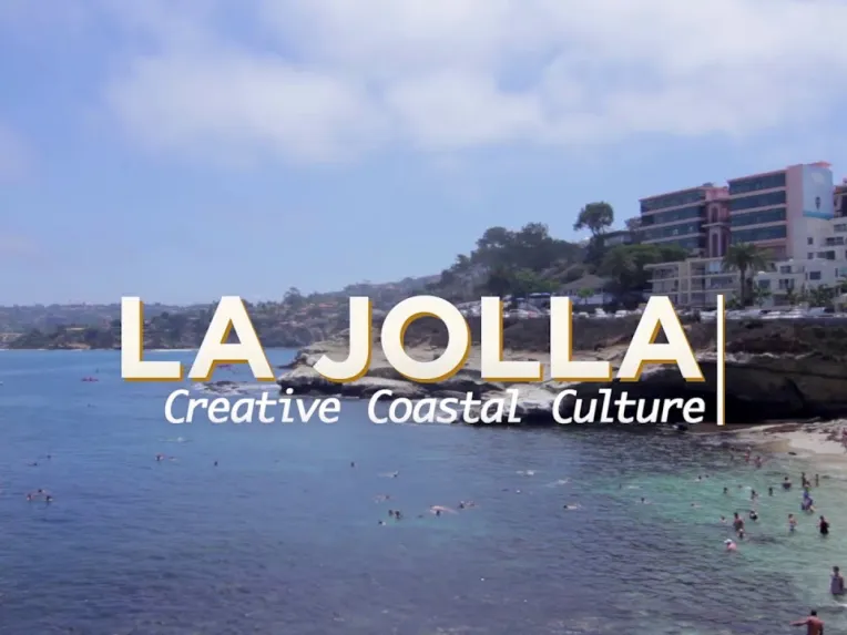 View of La Jolla coastline with people on the beach and buildings in the background; text overlay reads "LA JOLLA Creative Coastal Culture.