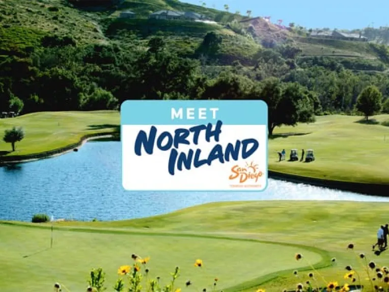 A golf course with a pond, green hills, and golfers; a sign in the center reads, "Meet North Inland San Diego.