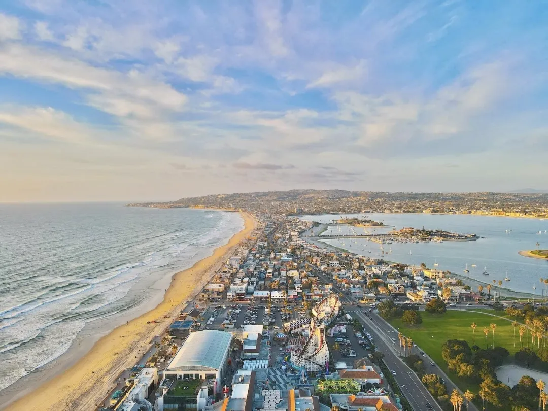 Aerial view of a coastline with a sandy beach and a coastal town under a blue sky.