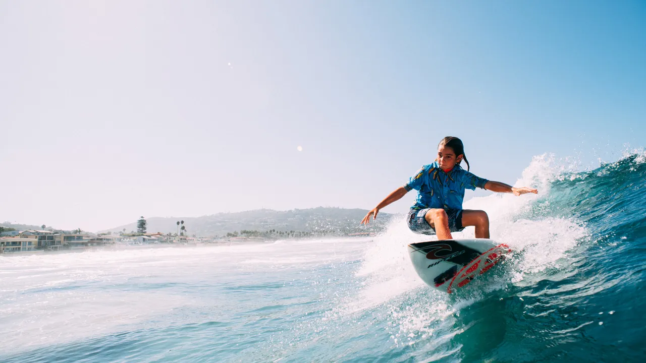 A surfer riding a wave with the coastline in the background