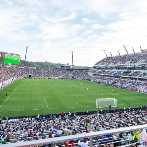 A large stadium filled with spectators watching a soccer match in progress on a clear day.