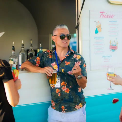 People chatting and enjoying drinks at a colorful outdoor bar in San Diego, with a casual social atmosphere and menu board visible in the background.