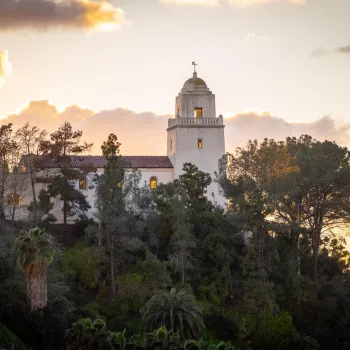 A sunset view of Presidio Park in San Diego, with the white adobe museum building in the foreground.