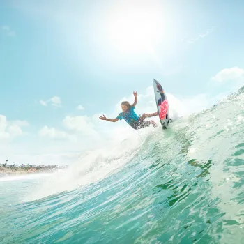 Young man catching an epic wave on a surfboard with a smile graphic in San Diego