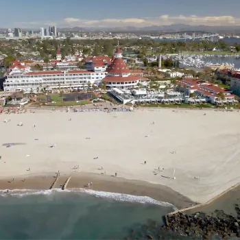 Aerial of Coronado Beach with the Hotel Del Coronado, Coronado Bay Bridge, and San Diego Skyline in the Background.