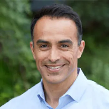 Gerry Granados with short dark hair, wearing a light blue collared shirt, smiling in front of a blurred green outdoor background.