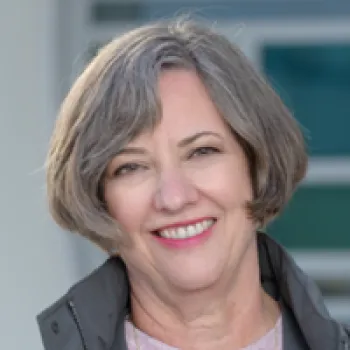 Martha Gilmer with short gray hair and a gray jacket smiles at the camera in an outdoor setting.