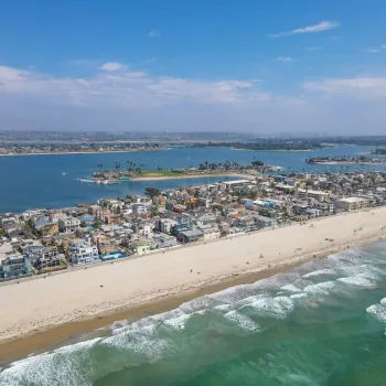 Aerial of Mission Beach boardwalk and waterfront houses and vacation rentals with Mission Bay in the background