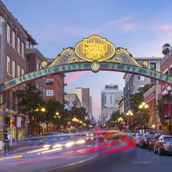The entrance arch to San Diego’s Gaslamp Quarter is shown over a busy street with blurred car lights and historic buildings at dusk.