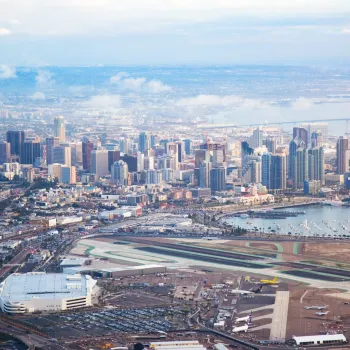 Aerial view of downtown San Diego with high-rise buildings, waterfront, and an airport runway in the foreground.