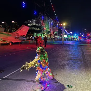 A figure draped in Christmas lights crouches on the deck of the USS Midway Museum during the Jingle Jets holiday event in beautiful San Diego.