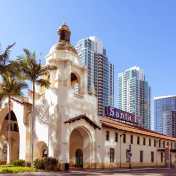 Historic Santa Fe Depot with Spanish-style architecture in front of modern high-rise buildings and palm trees under a clear blue sky.