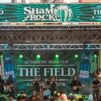 A band performs on an outdoor stage decorated with green banners for a ShamROCK event, featuring The Field Authentic Irish Pub in San Diego's Gaslamp Quarter.