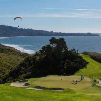 Golfers at Torrey Pines Golf Course overlooking the ocean with paragliders