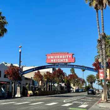 Neighborhood sign of University Heights of a red trolley overarching the main street of the neighbodhood