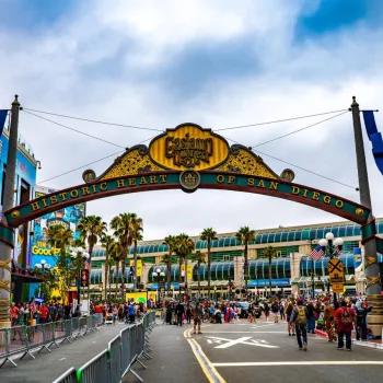 A large archway reading "Historic Heart of San Diego" stands over a busy street filled with people, with palm trees and buildings visible in the background, in San Diego's historic Gaslamp Quarter.