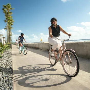 Two bicyclists ride along the Mission Beach boardwalk under sunny skies in beautiful San Diego.