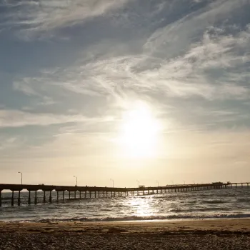Wide view of the Ocean Beach Pier in Ocean Beach, San Diego, silhouetted against a glowing sunset sky above the Pacific Ocean.