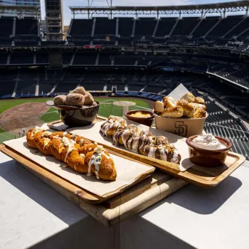 A plate of new Petco Park food offerings for 2026 is depicted against a backdrop of the San Diego ballpark.
