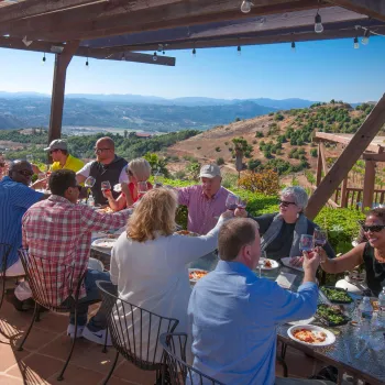 Group meeting taking place on an outdoor patio in San Diego's North Inland area, with attendees seated around a table enjoying food and conversation while overlooking rolling hills and a scenic valley.