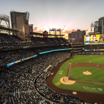 Petco Park stadium filled with Padres fans, overlooking the field at sunset with city skyline in background.