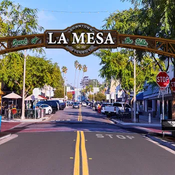 Colorful archway reading "LA MESA" over a tree-lined street with shops and palm trees.