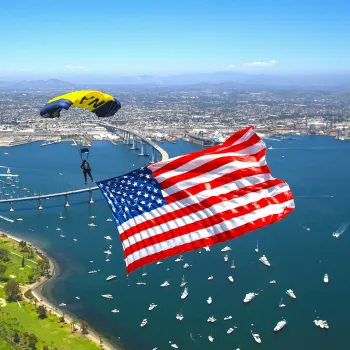 Skydiver descending with a large American flag over San Diego