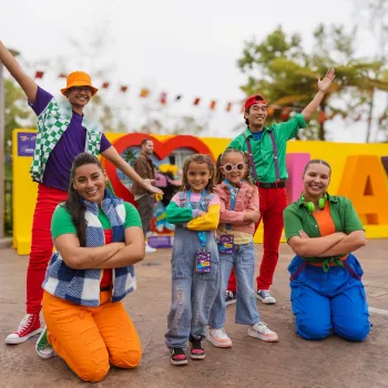 Six colorful characters posing joyfully in front of a vibrant sign at LEGOLAND California for the summer LEGO Festival.