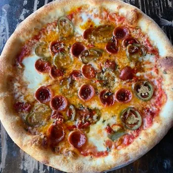 A pizza with pepperoni slices, jalapeño peppers, melted cheese, and tomato sauce on a rustic wooden surface.