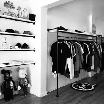 A clothing store interior with racks of shirts, shelves displaying hats and toys, and a rug with a graphic logo on a wooden floor.