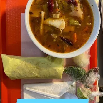 A bowl of 7 Mares seafood soup, a wrapped tortilla, lime wedges, and a plastic spoon on an orange tray.