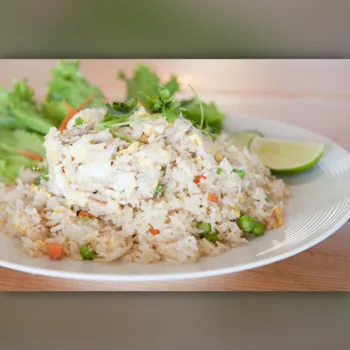 A plate of fried rice with crab meat, peas, carrots, and egg, served with lettuce, cilantro garnish, and a lime wedge on the side.
