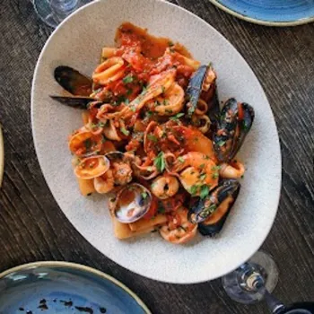 Oval plate of seafood pasta in red sauce, garnished with herbs, surrounded by other dishes on a wooden table.