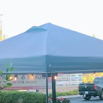 Two large gray tents set up in a parking lot with a black pickup truck parked nearby and storefront signs visible in the background.