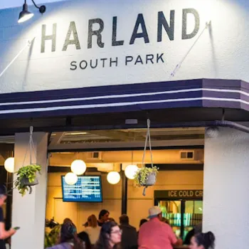 People sit outside and inside Harland South Park, a restaurant with a modern exterior, hanging plants, and glowing round lights.