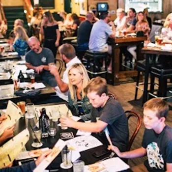 A busy restaurant with groups of people sitting at tables, eating, drinking, and talking in a lively, casual atmosphere.