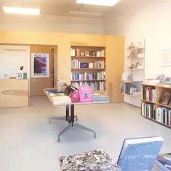 A small bookstore interior with bookshelves lining the walls, books displayed on tables, and soft lighting illuminating the space.
