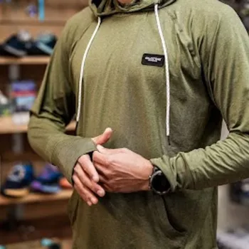 Person wearing a green long-sleeve athletic hoodie with thumbholes, adjusting the sleeve in a store with running shoes displayed in the background.