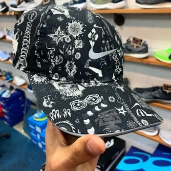 A hand holds a black and white patterned baseball cap featuring various abstract and geometric designs in a shoe store.