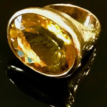 A gold ring featuring a large, oval-cut yellow gemstone displayed on a reflective black surface.